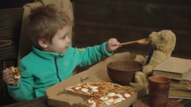 Diğer elinde kaşık ve Beklemeler pizza üzerinden bir ayı oyuncak çocuk beslemeleri. Çocuk ayı hakkında umurunda değil. Lezzetli pizza. Beslenme kavramı. Küçük çocuk oyuncak ayı besleme. Besleme ve oyuncak arkadaşım dikkat çekici çocuk.