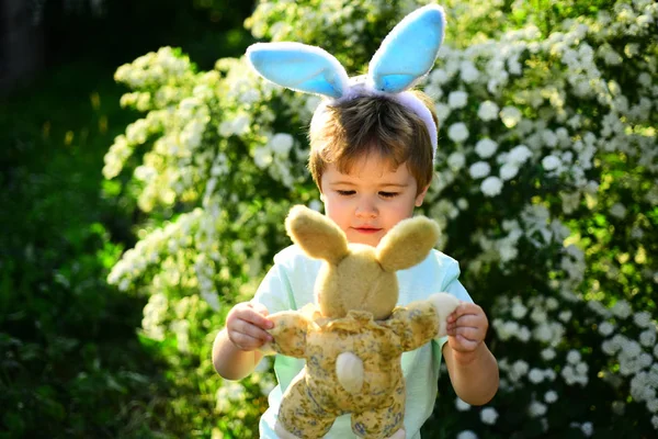 Um miúdo coelho com orelhas de coelho. Brinquedo de lebre. Caça ao ovo nas férias da primavera. Adoro Páscoa. Férias em família. Criança na floresta verde. Feliz Páscoa. Infância. Coelho com ovos de Páscoa — Fotografia de Stock