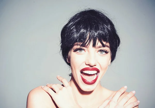 Woman with attractive red lips looks at camera. Lady in black wig with make up on grey background. Girl on happy smiling face posing with naked shoulders. Beautiful smile concept — Stock Photo, Image