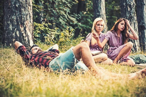 Stark kille liggande i gräset. Två tjejer läsa böcker intill lägerelden. Vänner camping i sommar — Stockfoto