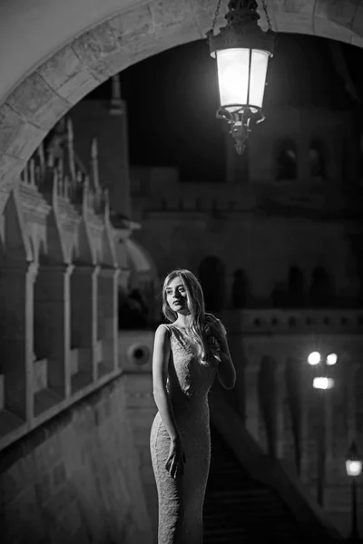 Sexy belle jeune femme à la mode en robe de soirée longue vue sur les lumières de la ville de nuit. Jolie dame aux cheveux longs . — Photo