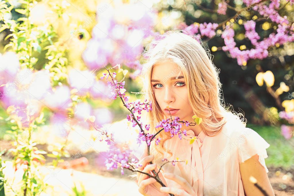 Beautiful blonde woman in blooming lilac garden, nature background. Young woman enjoy flowers in garden, defocused. Spring bloom concept. Lady walks in park on sunny spring day