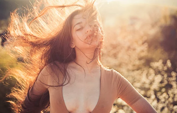 Mulher no rosto calmo desfrutar de dia ensolarado e ventoso, natureza no fundo, desfocado. Menina com decotado desfrutar de seu cabelo acenando pelo vento. A senhora parece atraente com o cabelo comprido acenando. Conceito de cuidados capilares — Fotografia de Stock