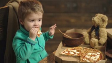Bir çocuğun bir ahşap arka plan üzerinde bir pizza yemek kapatın. Küçük çocuk bir dilim pizza üzerinde ahşap bakcground izole sahip. Sevimli çocuk evde pizza yemek.