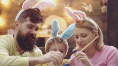 Anne, baba ve oğul resim yumurta vardır. Mutlu aile Paskalya için hazırlıyoruz. Sevimli küçük çocuk çocuk bunny kulaklar giyiyor. Ahşap arka plan üzerinde Paskalya yumurtaları.
