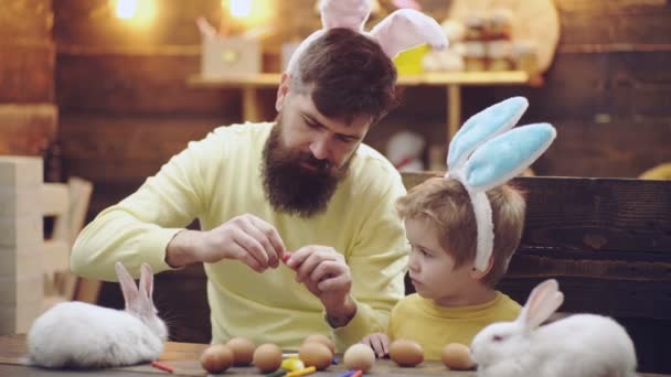 Glad påsk. En far och hans son måla påskägg. Lycklig familj förbereder för påsk. Söt liten barn pojke bär bunny öron på påskdagen. — Stockvideo