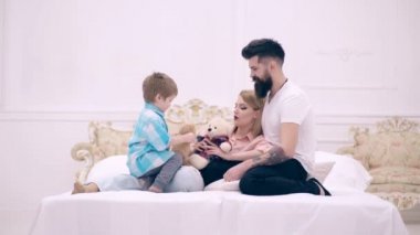 Çocuk, anne ve baba yatağa, otur gülümseyen ve iletişim. Genç mutlu çift birlikte yatak odasında. Genç aile evde oynak olmak. Mutlu aile ile yumuşak yastık evde yatakta.