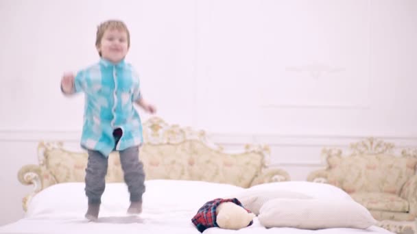 Feliz niño saltando en la cama en el dormitorio. lindo niño pequeño o niño pequeño saltando felizmente en casa. El niño rizado en la cama salta antes de irse a la cama. Niño es feliz y divertido en el dormitorio de los padres . — Vídeo de stock