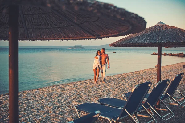 Aşk Denizi Adası'nda şemsiyelerle sahilde günbatımı yürüme çift. — Stok fotoğraf