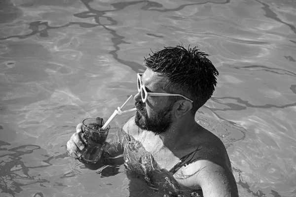 Fête de piscine avec hipster en eau bleue. Cocktail avec homme barbu dans la piscine. L'homme nage et boit du mojito alcoolisé. Détendez-vous en mer et station thermale. Vacances d'été à Miami Beach ou aux Maldives — Photo