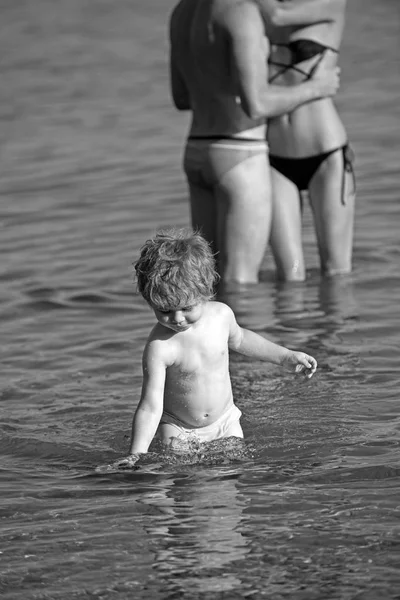 Mały chłopiec i para zakochanych w wodzie. mały chłopiec dziecko pływać w wodzie morskiej w lecie z rodzicami. — Zdjęcie stockowe