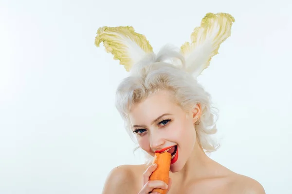 Hermosa mujer joven con orejas de conejo está comiendo zanahoria en el fondo de color. Vacaciones de Pascua . — Foto de Stock