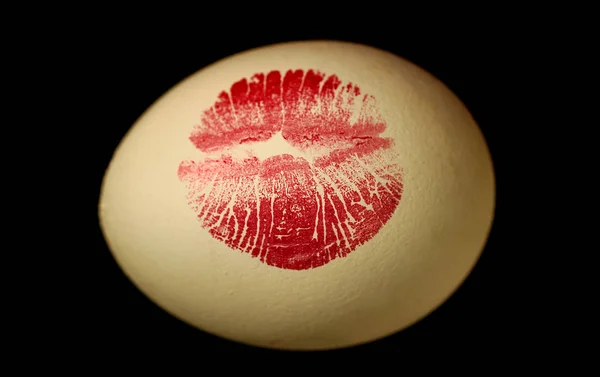 Red lip imprint on easter egg on black background. Print of red lips on white egg. Egg hunt.