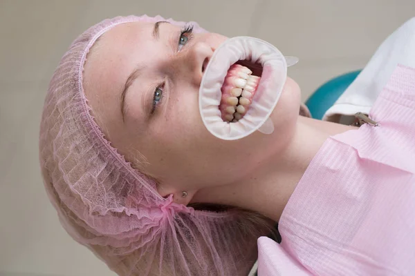 Menina bonita na cadeira dentária no exame no dentista. Mulher feliz sorrindo em um fundo abstrato com luzes embaçadas . — Fotografia de Stock