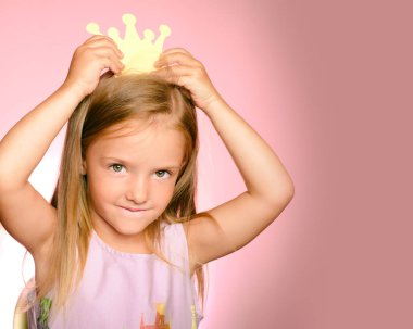 Altın taç küçük kraliçem. Küçük Prenses kız sarı taç ve pembe bir arka plan üzerinde güzel bir elbise. Güzel neşeli çocuk gerçek duyguları ifade etme. Metin için yer.