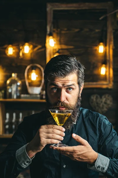 Barman hipster. Un hombre apuesto y pensativo sostiene un vaso de martini. Hombre guapo bebiendo alcohol mientras está sentado en el bar . — Foto de Stock