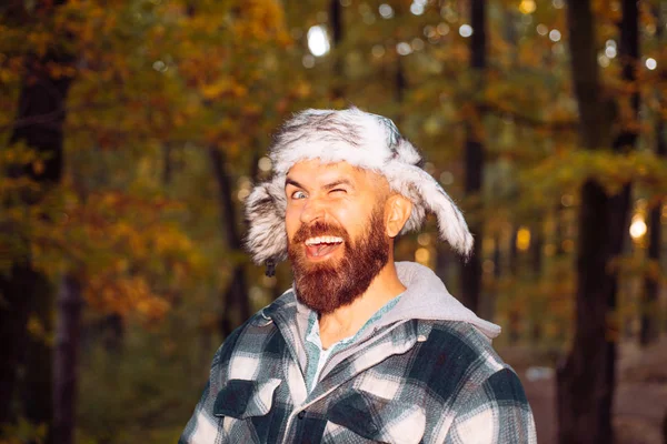 Young bearded man having fun outdoors. Portrait of a young bearded man in warm ethnic hat on autumn forest background. He smile and look on camera. Autumn happy people. — Stock Photo, Image