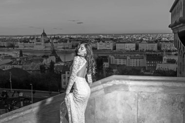 Şehvetli kadın balkonda, güzellik uzun saçlı. Şehir Manzaralı, moda akşam üzerinde beyaz gelinlik kadın. Gelin makyaj ile. Moda modeli stil ve saç modeli. Kız glamour bakışla