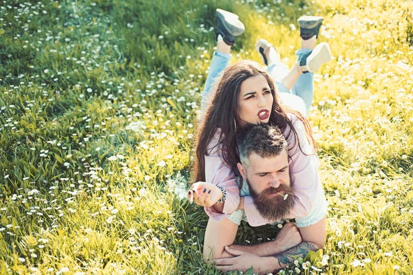 Conceito de hábito de fumar. Casal apaixonado passar o tempo ao ar livre e fumar. Homem e mulher deitado no dia de primavera grama. Casal em rostos rígidos fumar ao ar livre, natureza no fundo . — Fotografia de Stock