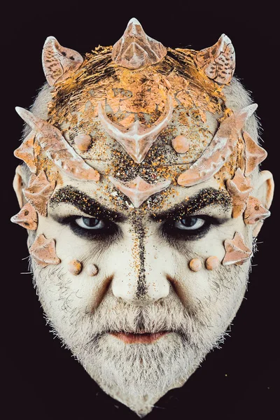 Head with thorns or warts, face covered with glitters, close up. Demon on serious face, black background. Alien, demon, sorcerer makeup. Senior man with beard, with monster makeup. Fantasy concept.