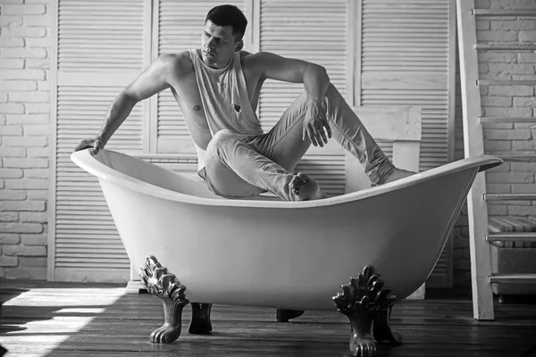 Мужчина в ванной, гигиена. Сексуальный мачо в танковом топе и джинсах. Парень сидит на ванне. Модель с крепким телом. Концепция гигиены и купания — стоковое фото