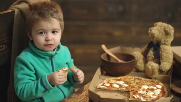 Fechar de menino bonito comendo pizza. O rapaz come uma pizza deliciosa. Deliciosa pizza italiana no fundo de madeira . — Vídeo de Stock
