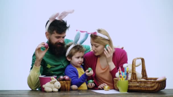 Mor, far och son är målning ägg. Lycklig familj förbereder för påsk. Söt liten barn pojke bär bunny öron. Påskägg på trä bakgrund. Påsk, familj, semester och barn koncept. — Stockvideo