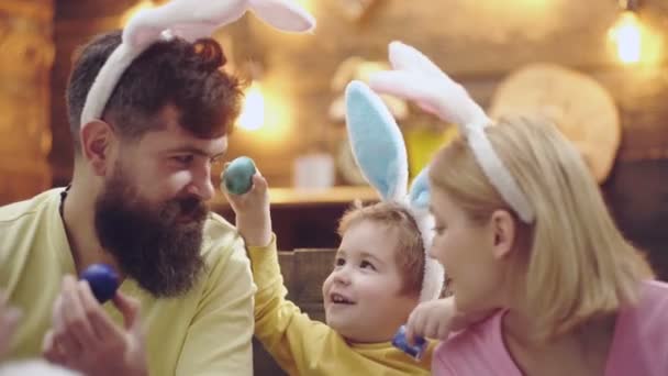 Primer plano de la madre, el padre y su hijo pintando huevos de Pascua. Familia feliz preparándose para la Pascua. Retrato de una familia que se ríe y pinta huevos de Pascua sobre un fondo de madera . — Vídeos de Stock