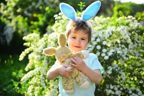 Маленький хлопчик у зеленому лісі. Щасливого Великодня. Дитинство. Полювання на яйця на весняні канікули. Кролик з кролячими вухами. Заєць іграшка. Люблю Великдень. Сімейне свято. Весняні свята — стокове фото