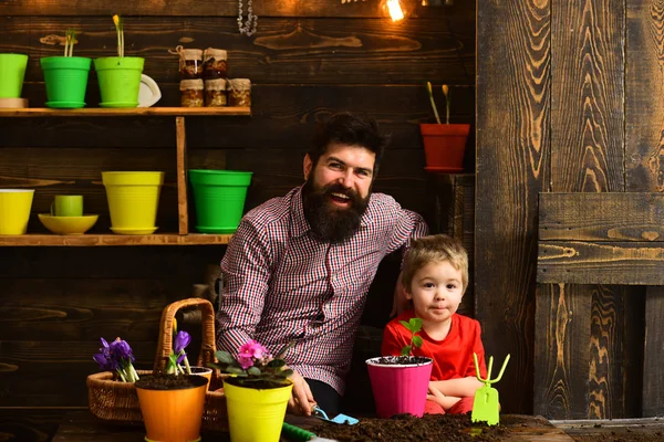 髭の男と小さな男の子は、自然を愛する。春の花を持つ幸せな庭師。花のケアに水をまきます。土壌肥料。家族の日。温室効果。父と息子。彼は花についてのすべてを知っています。 — ストック写真