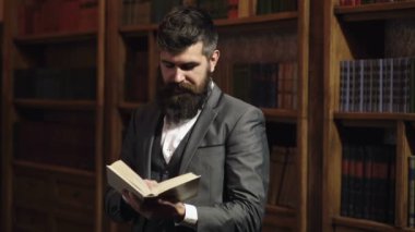 Eğitim, öğrenme, eğitim, araştırma, tarih, edebiyat konsepti. Öğrenci klasik kütüphanede duruyor ve elinde kitap tutuyor. Akıllı takım elbiseli sakallı adam kitaplığın yanında okuyor. Ciddi yüzlü ve uzun sakallı bir adam..