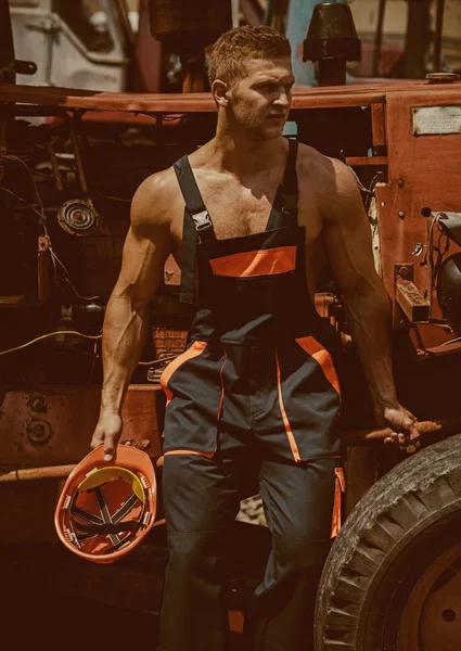 Worker concept. Strong worker rest at heavy construction machine. Handsome worker in working uniform at tractor cabin. Confident worker man at backhoe loader