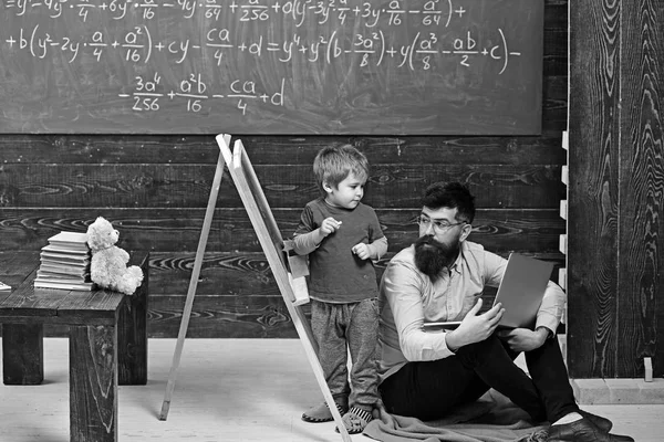 Profesor revisando el trabajo del estudiante en pizarra. El hombre que trabaja en el portátil habla con un niño pequeño. Concepto educativo — Foto de Stock