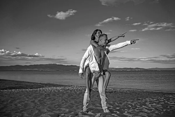 Ein Kerl trägt ein Mädchen auf dem Rücken am Strand im Freien. — Stockfoto