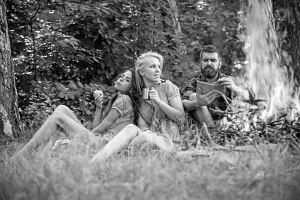 森でのキャンプの友人のグループです。男は火によって本を読んで。彼女の友人は、青リンゴを食べながら、マグカップからお茶を飲む金髪美少女 — ストック写真