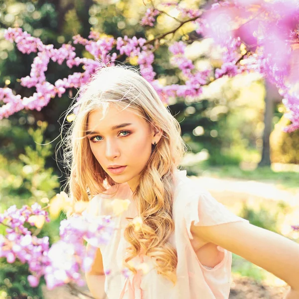 Девушка на мечтательном лице, нежная блондинка возле фиолетовых цветов иудейского дерева, природный фон. Весенний цветок. Леди гуляет в парке в солнечный весенний день. Молодая женщина наслаждается цветами в саду, обезжиренный . — стоковое фото