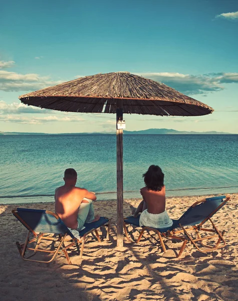 Jovem casal sentados juntos em uma areia por mar e olhando para um horizonte . — Fotografia de Stock