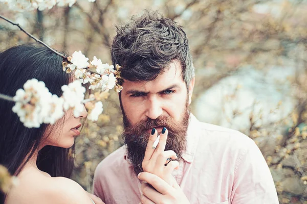 Пара курящих возле цветущих деревьев. Женские руки держат сигарету для мужчины в саду в весенний день. Пара влюбленных проводят время в весеннем саду, ветви с цветами на заднем плане. Концепция курения . — стоковое фото