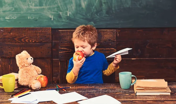 Kid eating apple with pleasure. Cute boy biting fruit with his eyes closed. Infant playing with paper plane