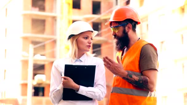 Retrato de los ingenieros de construcción que trabajan en la obra. Ingenieros en el sitio de construcción mirando los planos y discutiendo el proyecto. Trabajadores masculinos y femeninos en cascos en la zona del edificio . — Vídeos de Stock