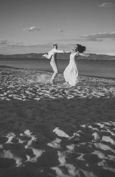 Homme et femme dansant, couple heureux en vacances. Couple amoureux courant sur la plage, au bord de la mer. Couple amoureux tient la main, avoir du plaisir, fond de mer et skyline. Lune de miel, concept de mariage . — Photo
