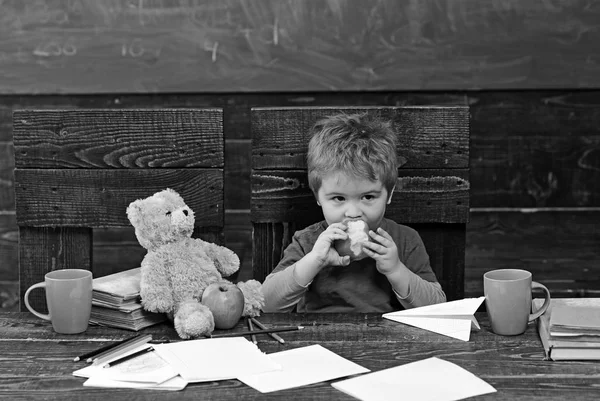 Σχολικές διακοπές. Πεινασμένο παιδί δάγκωμα Μήλου στην τάξη. Μικρό αγόρι παίζει με αεροπλάνο χαρτί και αρκουδάκι — Φωτογραφία Αρχείου