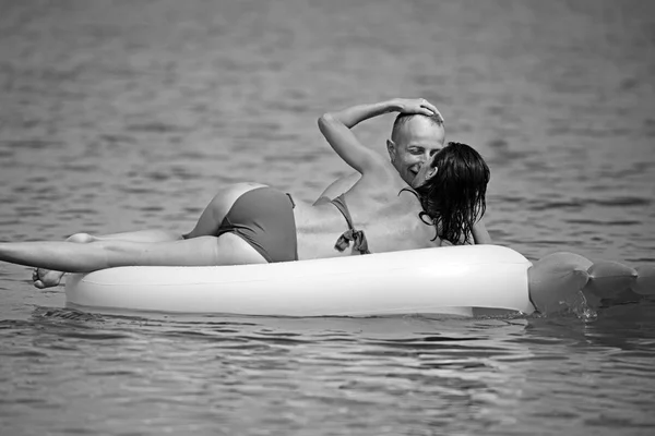 Homem e mulher em lua de mel, nadar em colchão em forma de abacaxi no mar. Feliz casal jovem nadando e rindo no colchão de ar. Conceito de férias de casal. Acessórios de verão para descanso colchão amarelo — Fotografia de Stock