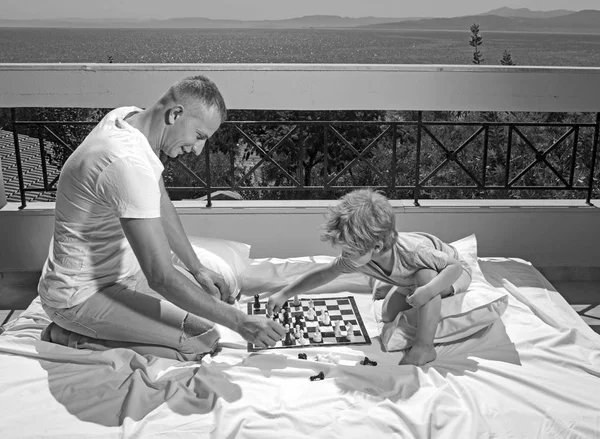 父の日に子供と一緒に家族での休暇。子供は父親とチェスします。幸せな家族の夏の旅行。バルコニーで息子と父は、チェスをプレイします。愛と家族の価値観と信頼 — ストック写真