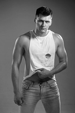 Adam seksi kolsuz bluz ve kot gri arka plan üzerinde. Adam pazı ve triceps ile kas el ile
