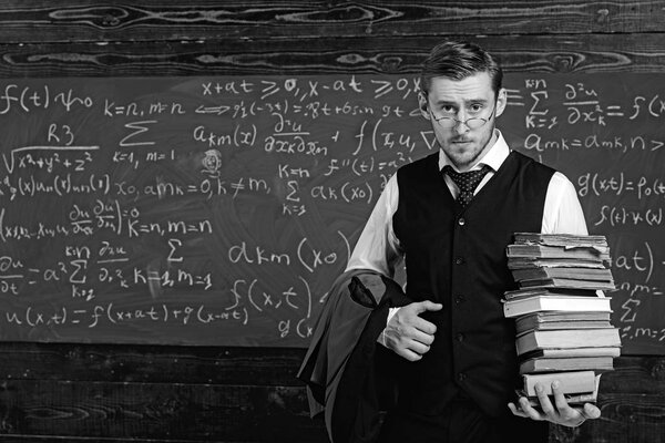 Young student in suit and glasses walking to library with heap of books. Bookworm studying for exam