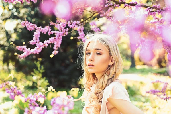 Lente bloei concept. Meisje op dromerige gezicht, tedere blonde in de buurt van violette bloemen van judas boom, natuur achtergrond. Lady wandelingen in het park op zonnige lentedag. Jonge vrouw genieten van bloemen in de tuin, intreepupil. — Stockfoto