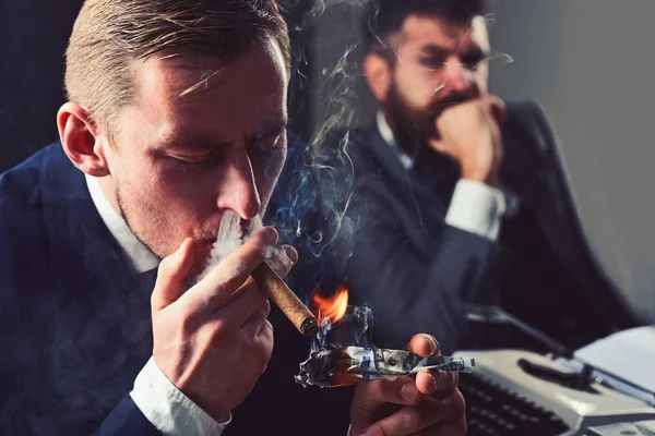 Waste of money. Man light up cigar from dollar banknote. Rich man smoking during business meeting. Businessmen have money to burn. Business partners writing financial report. Filthy with money