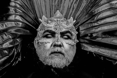 Adam dikenler veya siğiller ile yüz pırıltılar ile kaplı. Şeytan siyah zemin üzerine altın yakalı. Fantezi kavramı. Beyaz sakallı komuta sizde canavar gibi giyinmiş. Uzaylı, iblis, büyücü makyaj.