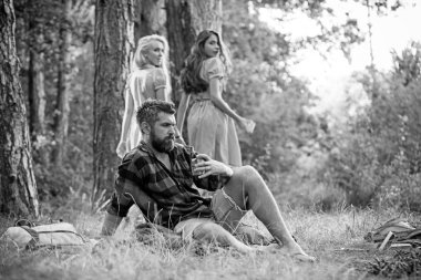 Güneşli çayır kamp. İki kız geri çim üzerinde oturan adam bakıyor. Acımasız adam kamp ateşi ile kahve içme